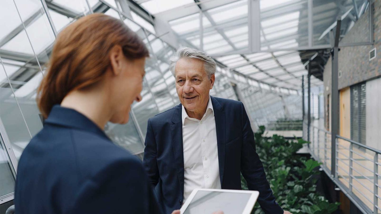 Zwei Geschäftspersonen im Gespräch, die Frau hält ein Tablet, der Mann steht vor einem offenen, lichtdurchfluteten Gang. © Westend61 / Westend61 via Getty Images © Westend61 / Westend61 via Getty Images