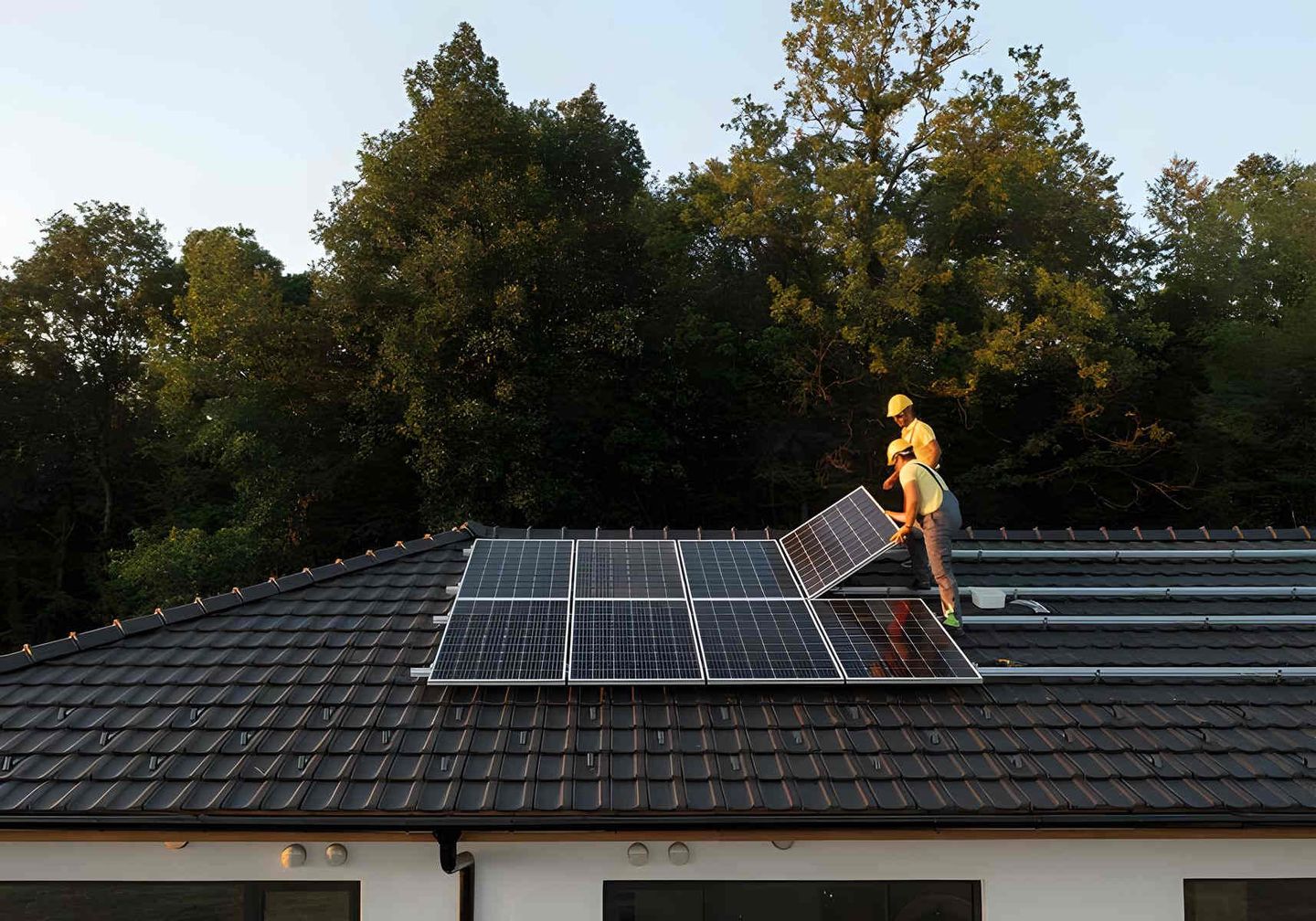 Zwei Arbeiter installieren Sonnenkollektoren auf dem Dach eines Hauses.