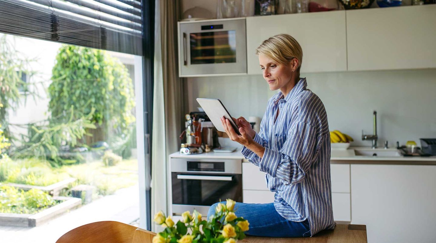 Eine junge Frau sitzt auf dem Küchentisch und informiert sich auf ihrem Tablet über die Verbrauchsrecherche. © Halfpoint Images / Moment via Getty Images