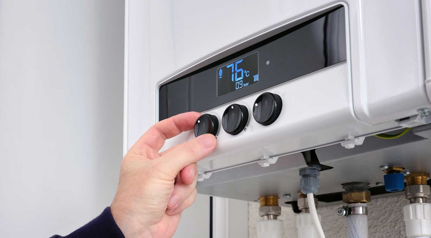 Eine Person stellt die Temperatur ihrer Gasheizung ein. © SergeyKlopotov / iStock/ Getty Images Plus via Getty Images