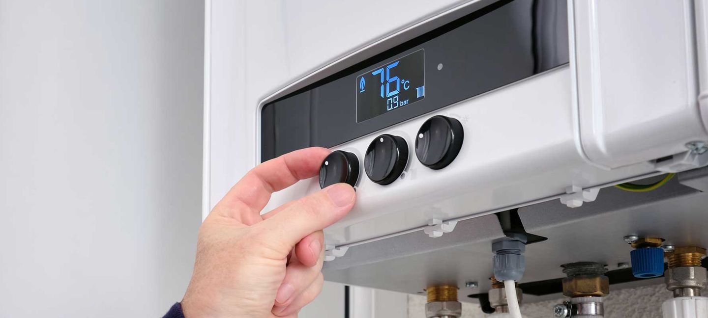 Eine Person stellt die Temperatur ihrer Gasheizung ein. © SergeyKlopotov / iStock/ Getty Images Plus via Getty Images