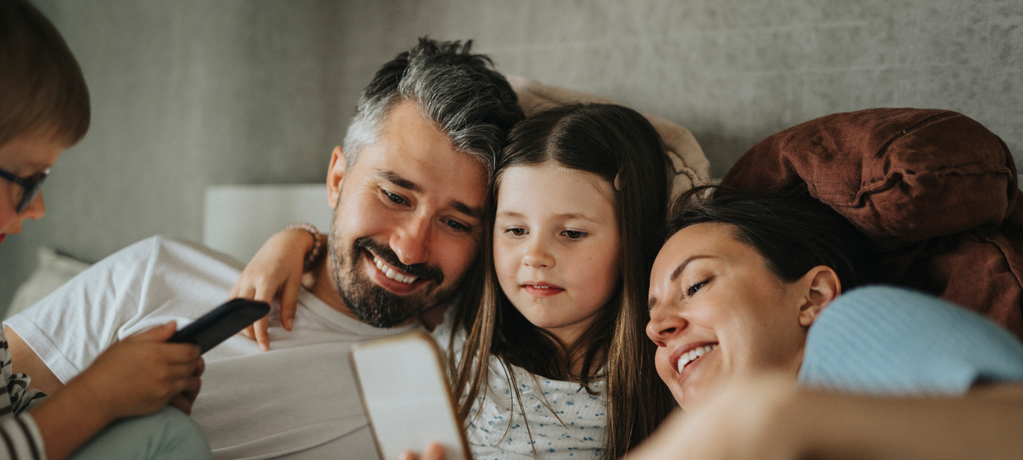 Eine Familie sitzt auf der Couch und schaut aufs Smartphone © Maskot / Maskot via Getty Images
