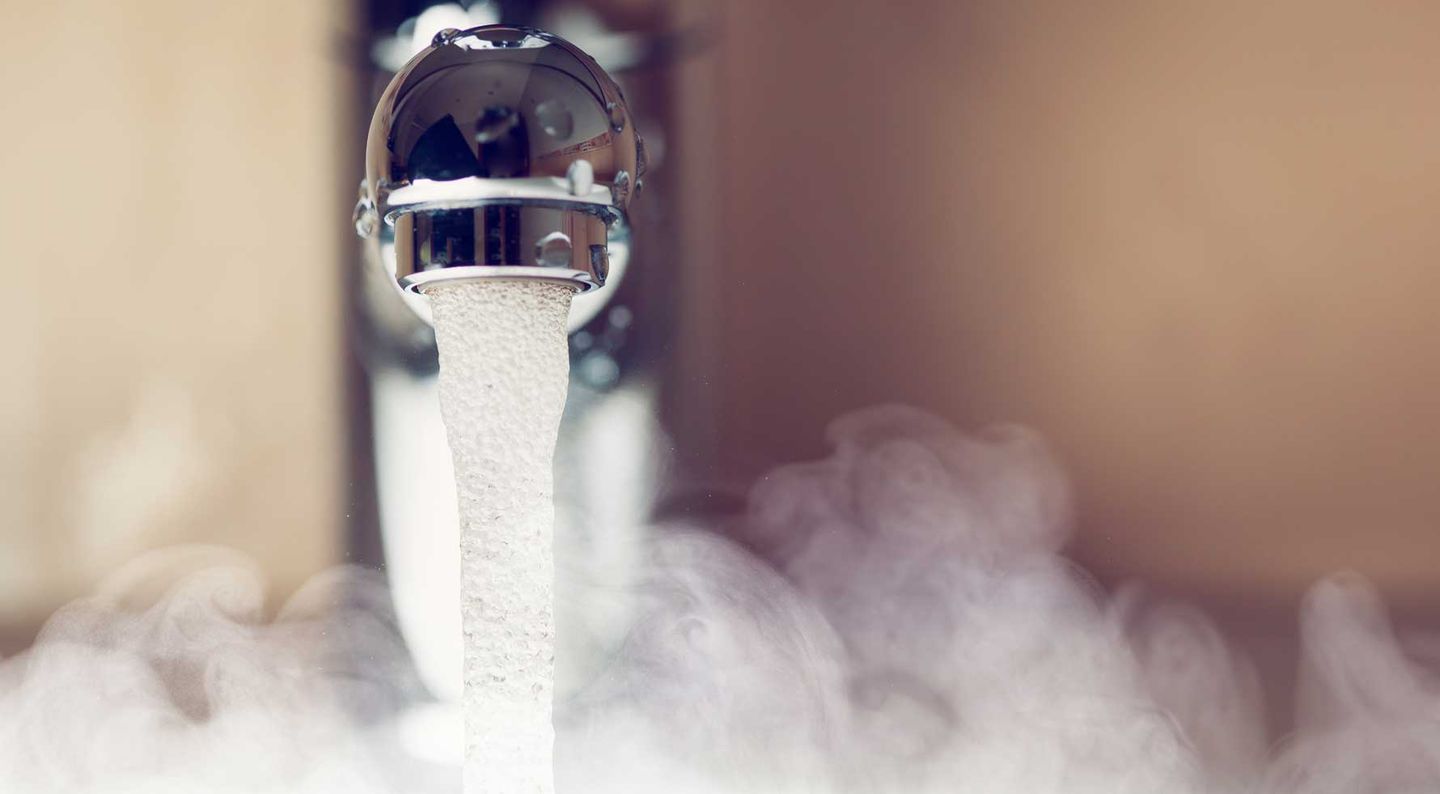Nahaufnahme eines Wasserhahns, aus dem warmes Wasser fließt, umgeben von aufsteigendem Dampf © nikkytok / iStock / Getty Images Plus via Getty Images