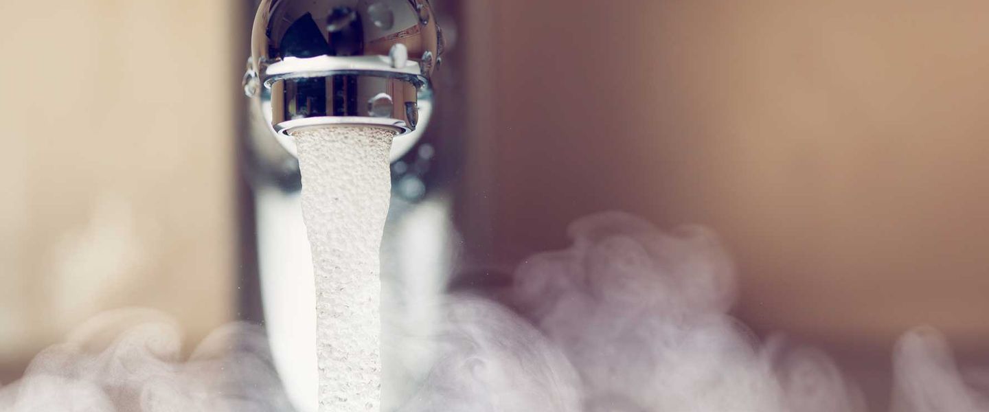 Nahaufnahme eines Wasserhahns, aus dem warmes Wasser fließt, umgeben von aufsteigendem Dampf © nikkytok / iStock / Getty Images Plus via Getty Images