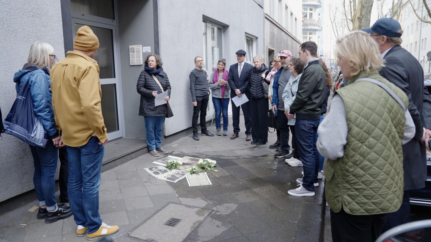 Eine Gruppe steht um eine Historikerin der Mahn- und Gedenkstätte Düsseldorf bei Stolpersteinen, die mit Rosen und Fotos geschmückt sind. © Stadtwerke Düsseldorf