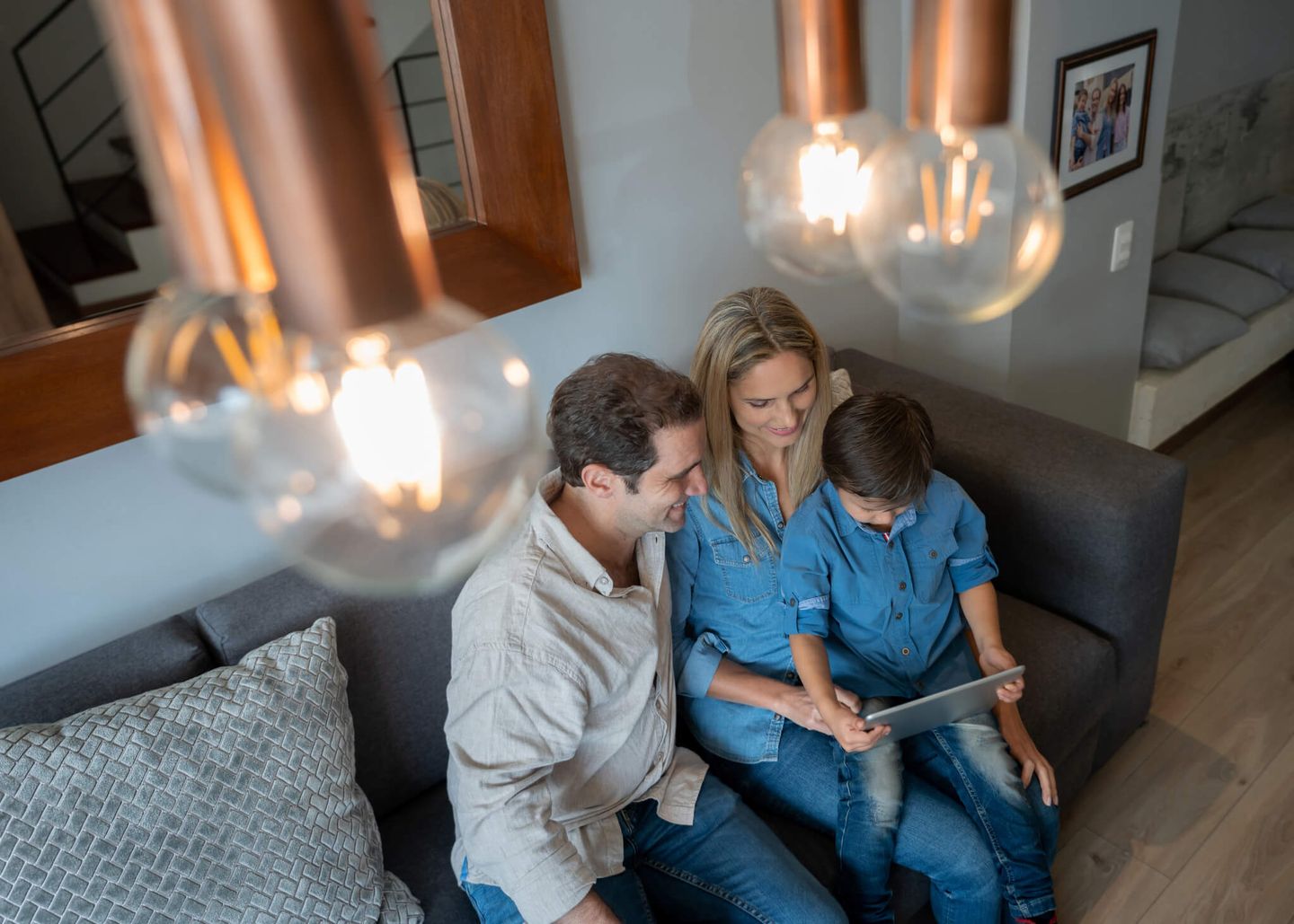Eine glückliche Familie sitzt zuhause auf dem Sofa und schaut gemeinsam auf ein Tablet.