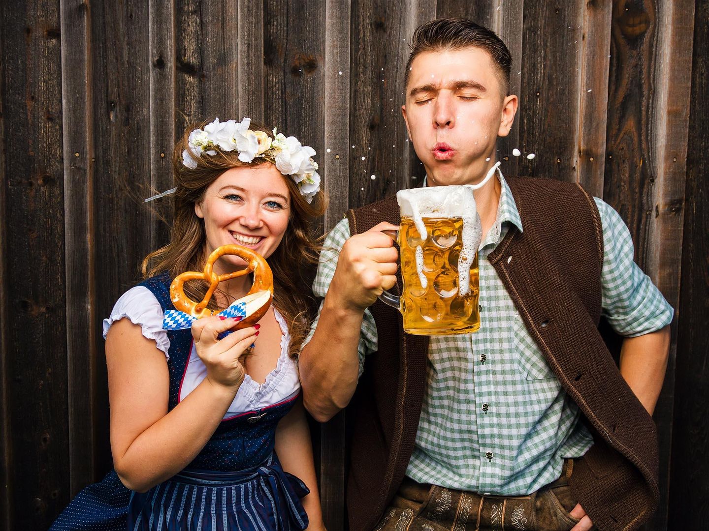 Zwei feiernde Personen in Tracht und bayrischen Spezialitäten