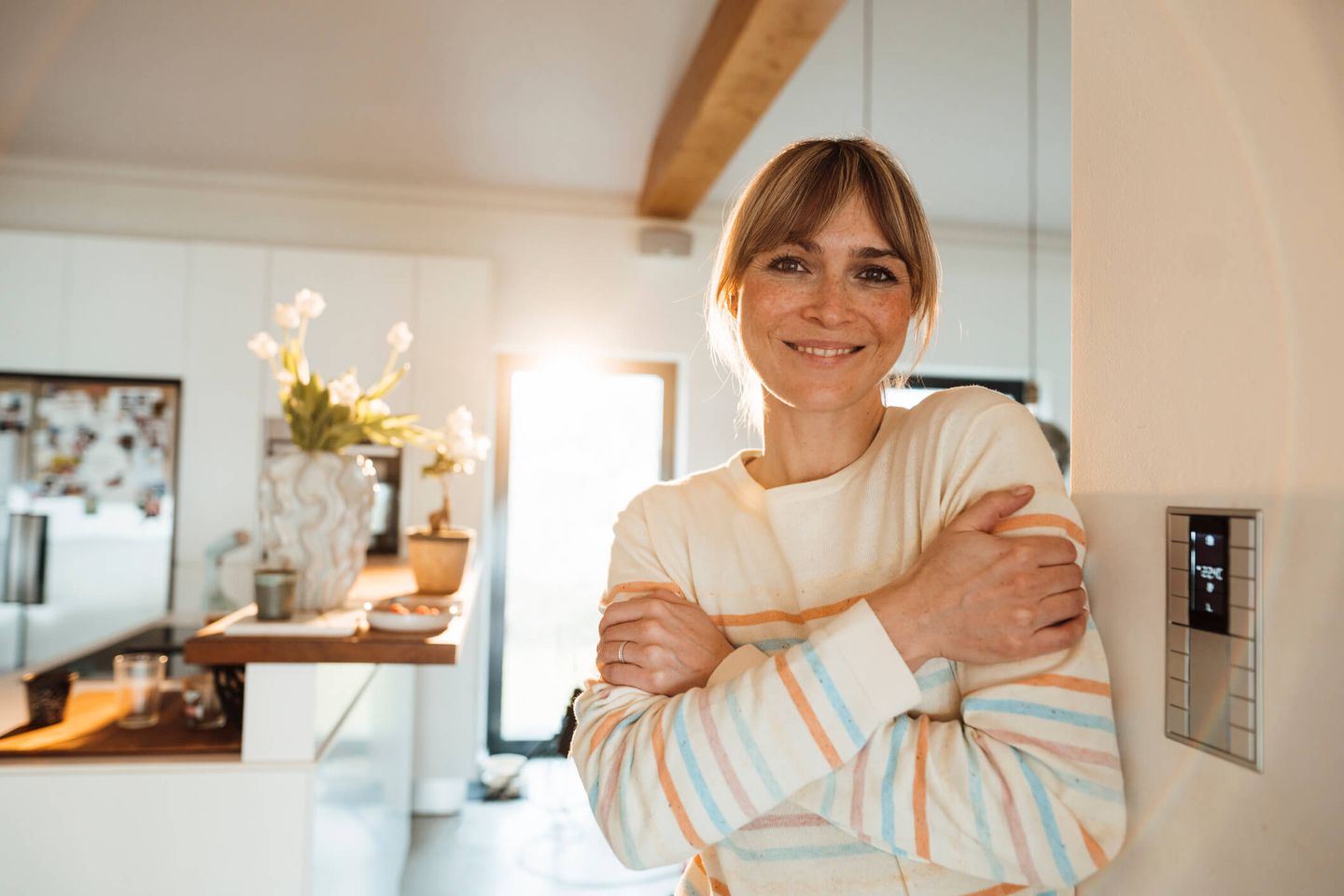 Eine Frau lehnt entspannt an der Wand und freut sich über wohlige Wärme – neben ihr ein digitales Thermostat. © Westend61 / Westend61 via Getty Images
