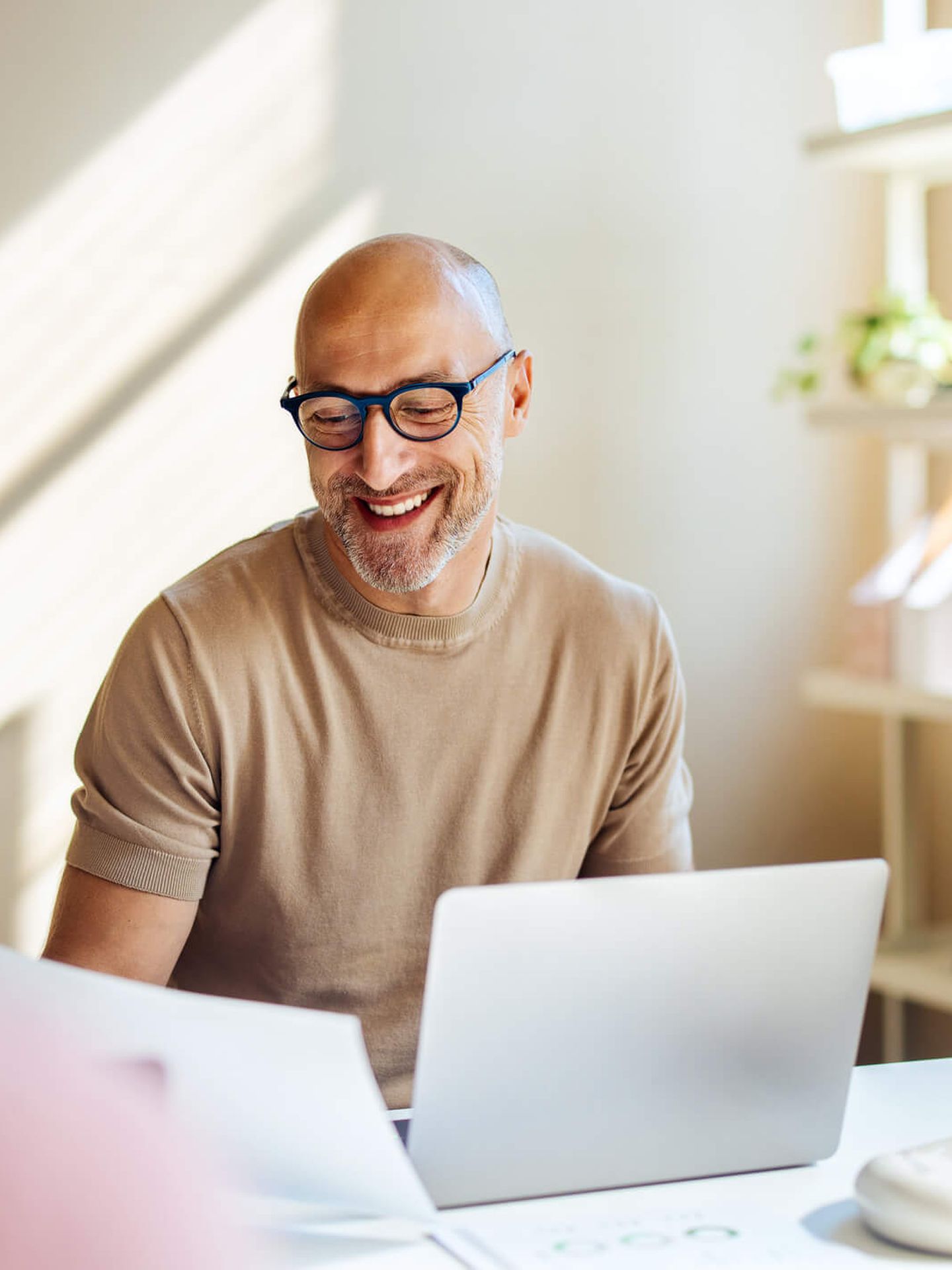 Ein Mann sitzt lächelnd an seinem Schreibtisch. © FreshSplash / iStock / Getty Images Plus via Getty Images