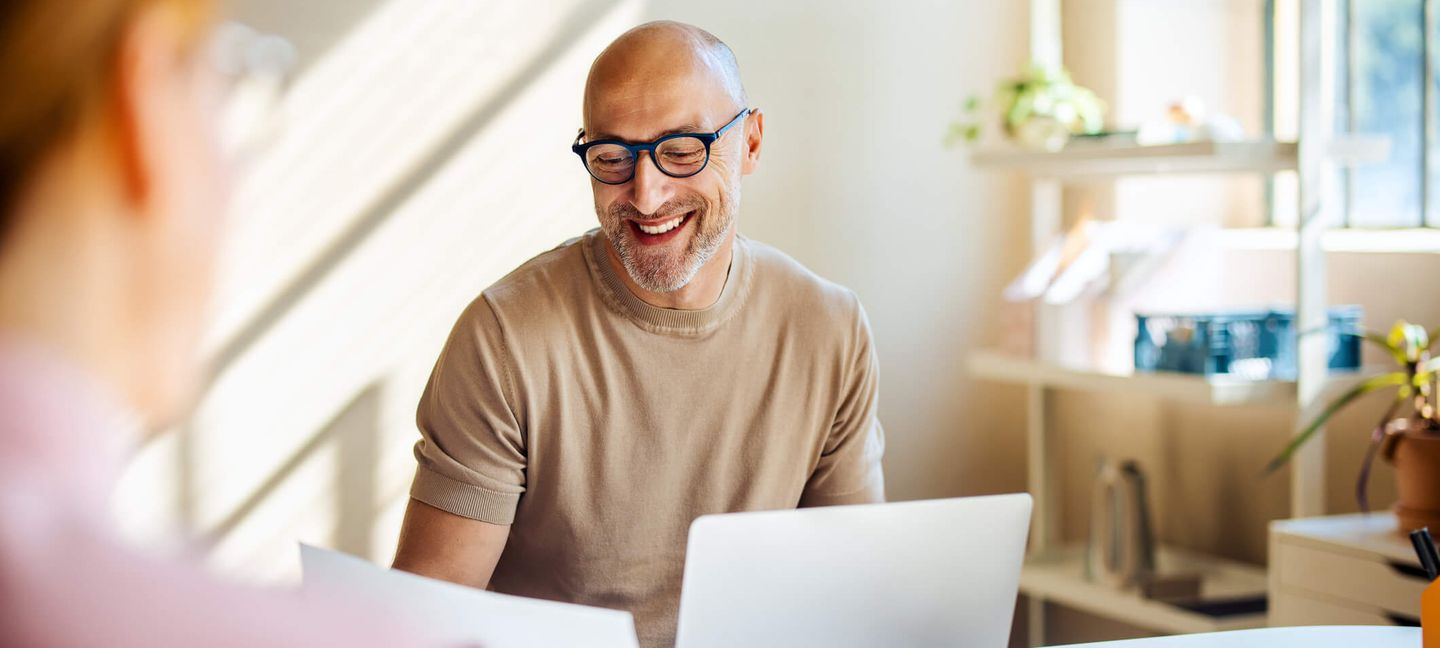 Ein Mann sitzt lächelnd an seinem Schreibtisch. © FreshSplash / iStock / Getty Images Plus via Getty Images