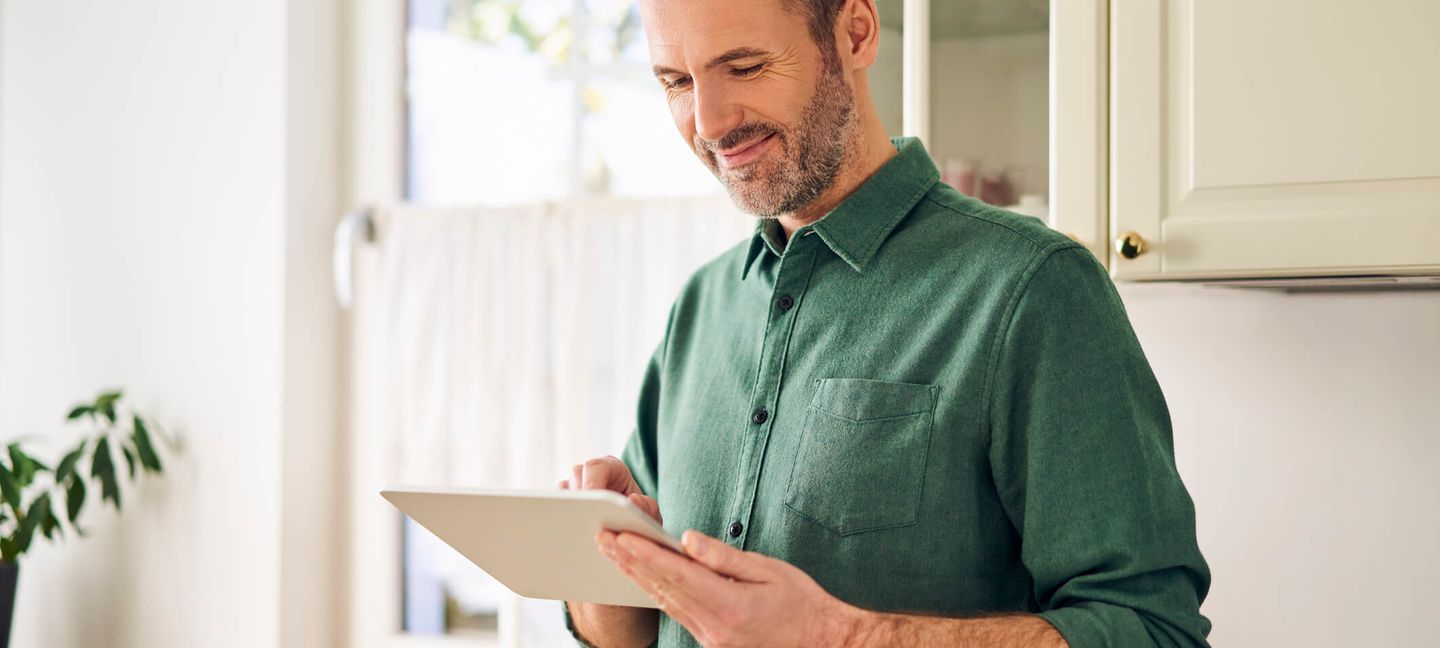 Mann steuert sein Home Energy Management System (HEMS) über ein Tablet in seiner Küche. © Westend61 / Westend61 via GettyImages