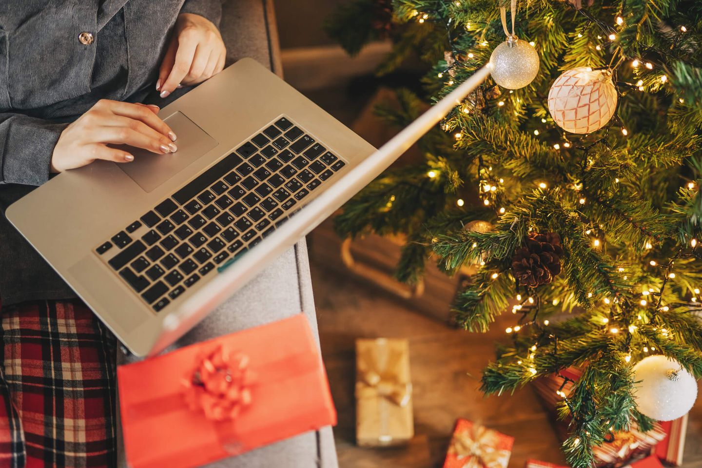 Ein Laptop auf einer Couch-Rückwand, daneben steht ein Weihnachtsbaum mit Geschenken. © Kseniya Ovchinnikova / Moment via Getty Images