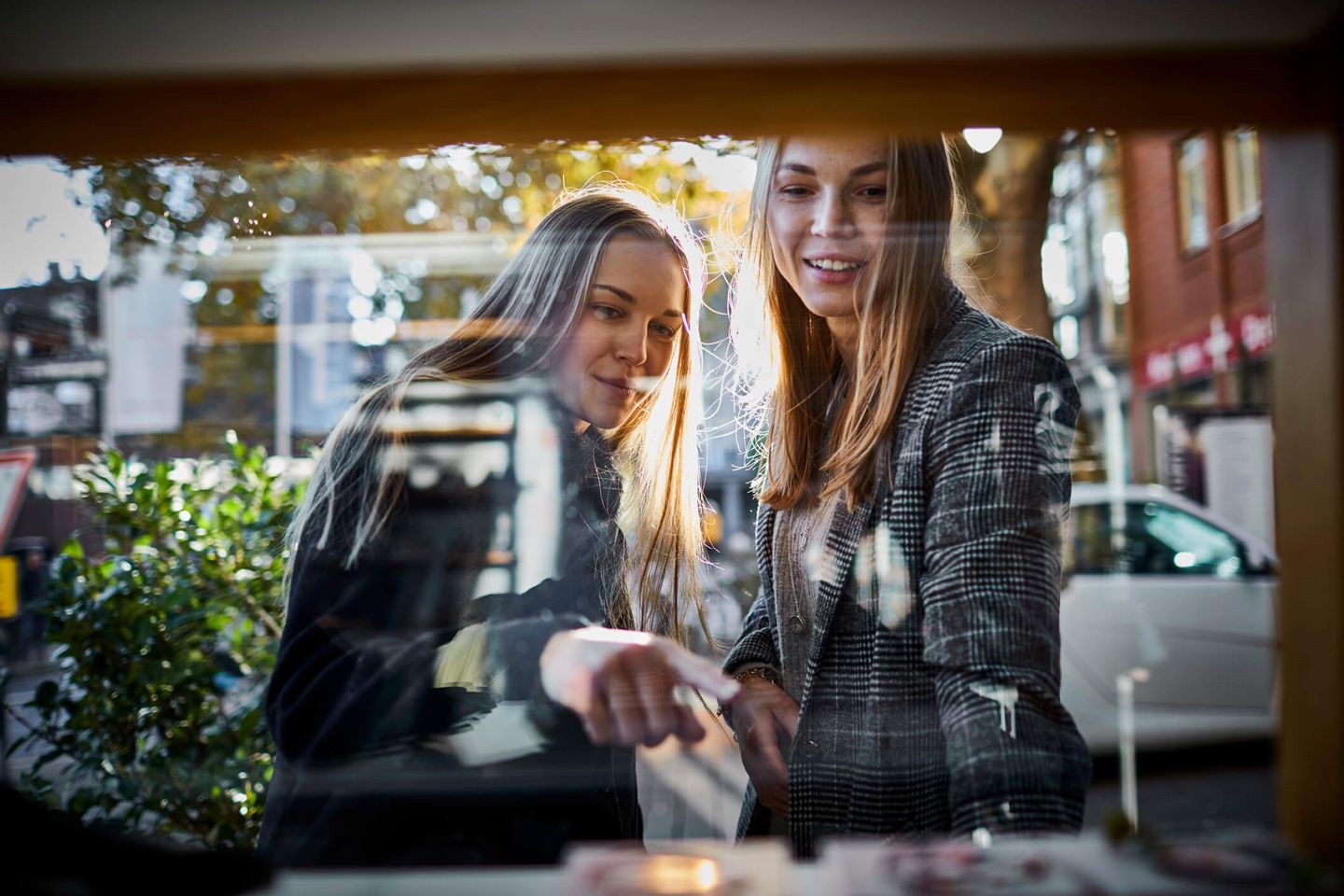 Zwei Mädchen stehen vor einem Schaufenster, eine von ihnen zeigt auf ein Produkt hinter der Scheibe. © Oliver Rossi / Stone via Getty Images