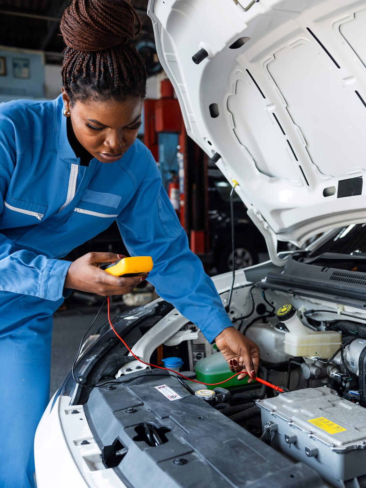 Eine Frau in blauem Overall wartet ein E-Auto, dessen Motorhaube geöffnet ist. © panaya chittaratlert / E+ via Getty Images