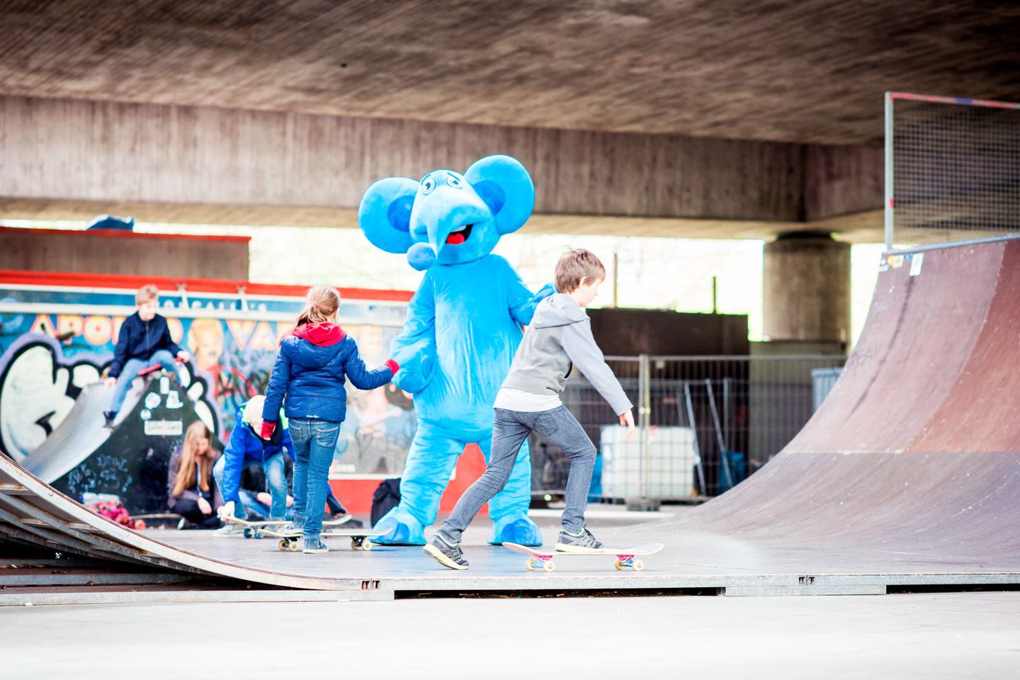 Der Blaue Elefant spielt mit Kindern auf einem Skateplatz.