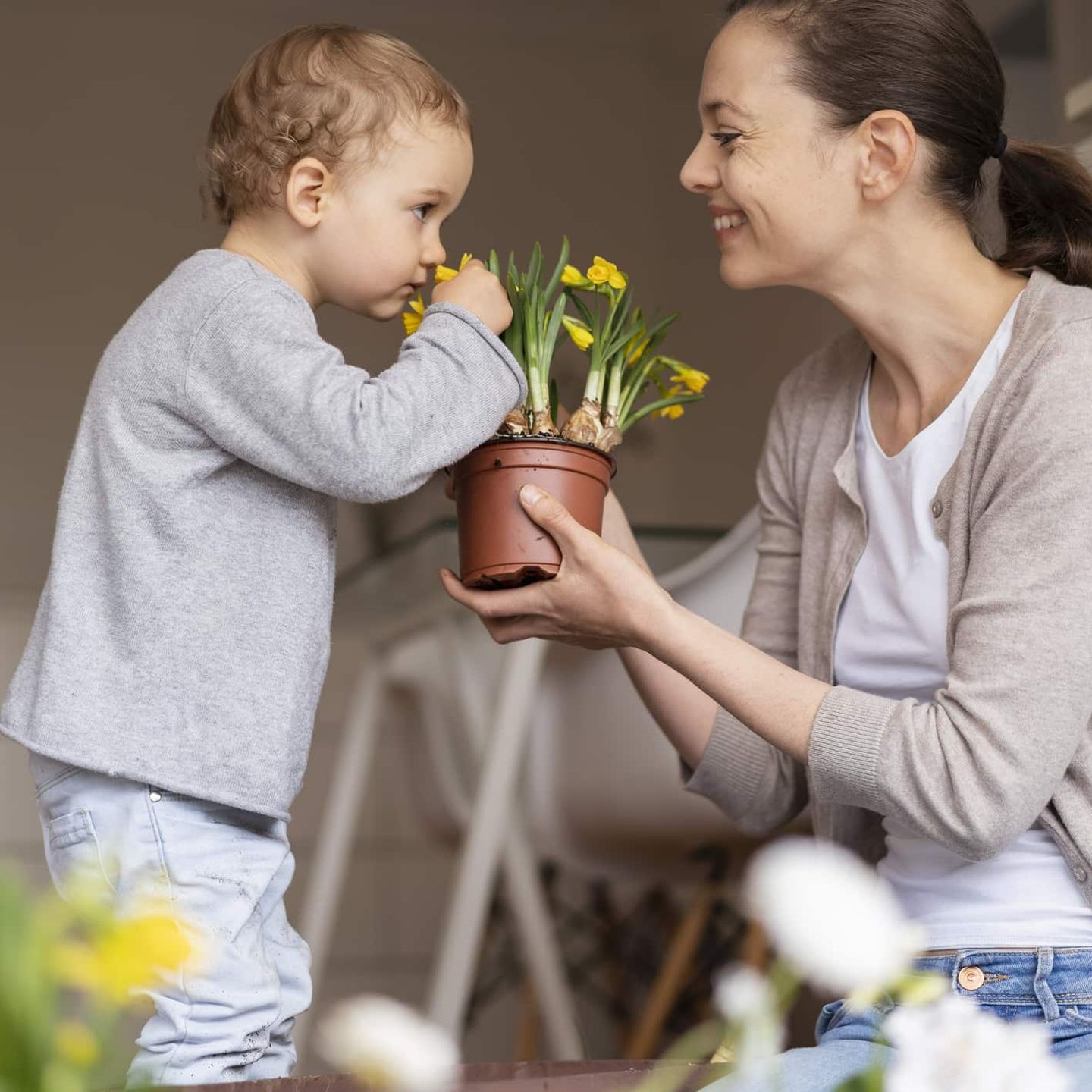 Mutter hält Topf mit gelben Blumen, während ihr Kind daran riecht.