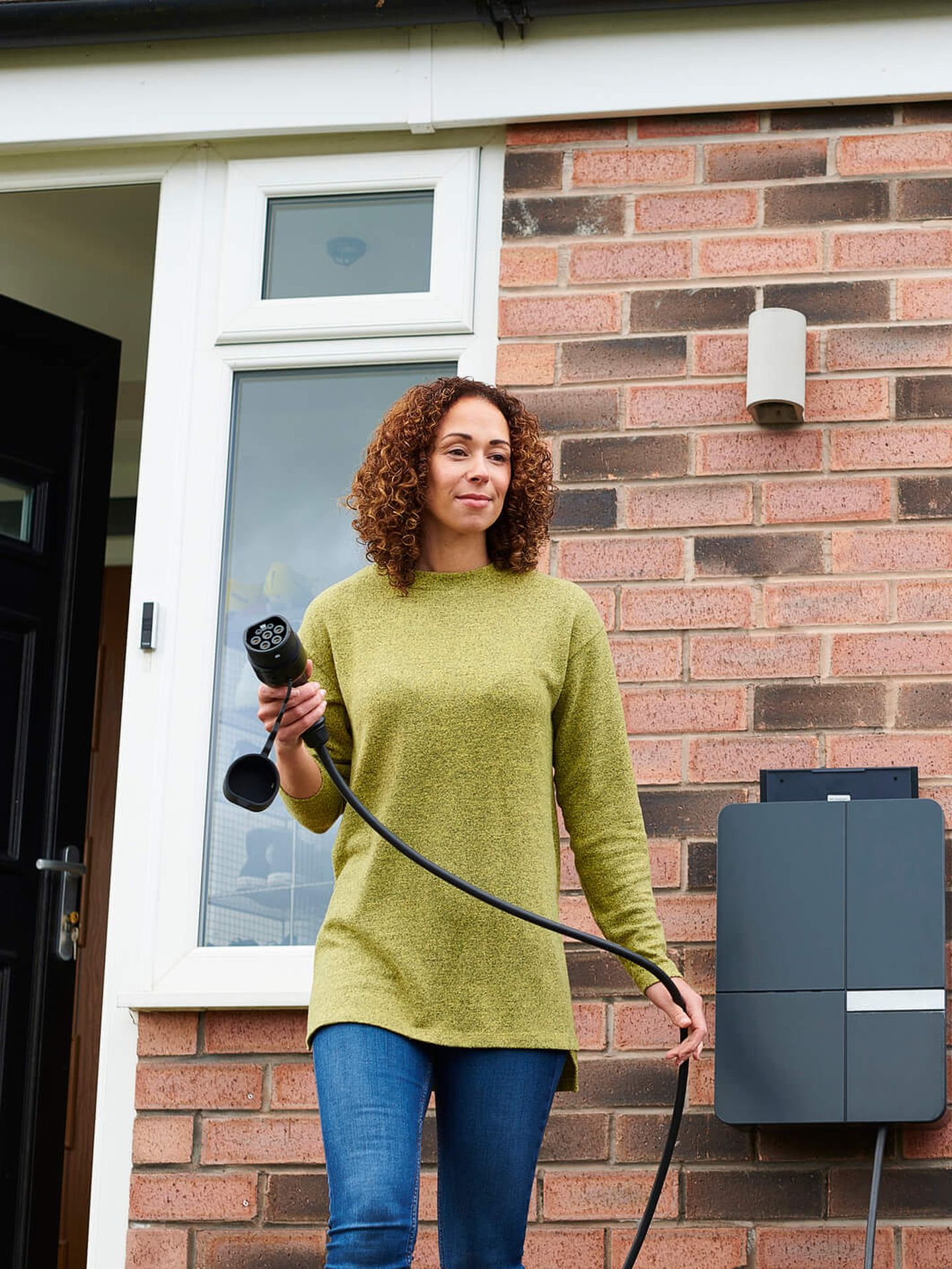Eine junge Frau auf dem Weg, ihr E-Auto an eine private Ladestation anzuschließen. © sturti / E+ via Getty Images © sturti / E+ via Getty Images