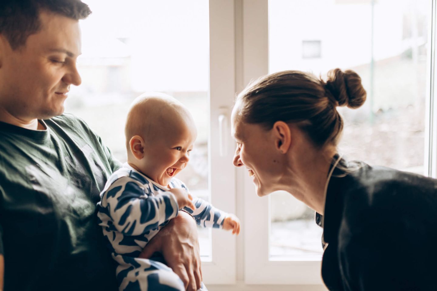 Ein Ehepaar sitzt mit ihrem lachenden Baby auf dem Boden vor einem sonnengefluteten Fenster