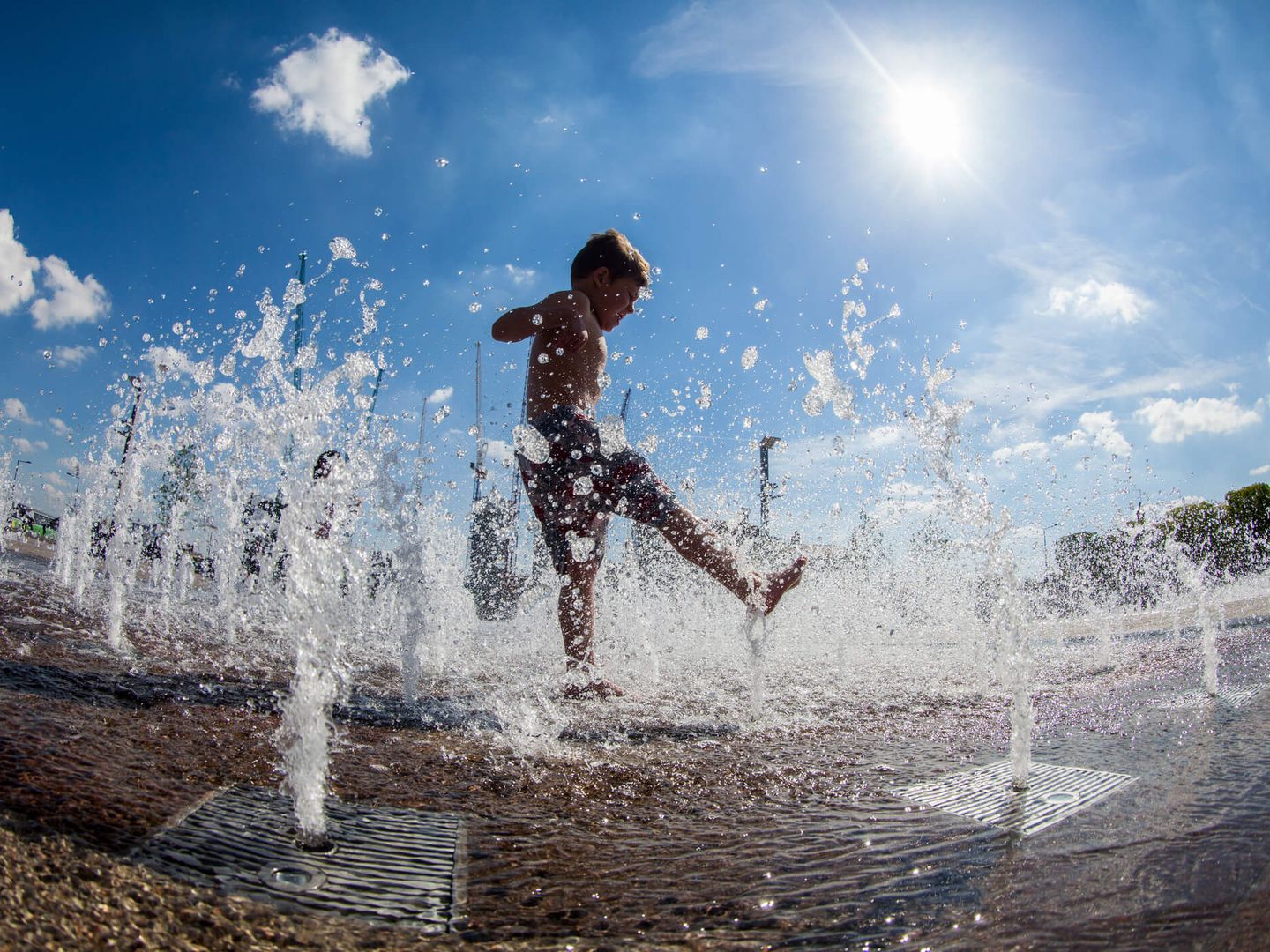Kind spielt in Wasserfontänen auf einem Platz bei strahlendem Sommerwetter.  © paul mansfield photography / Moment via Getty Images