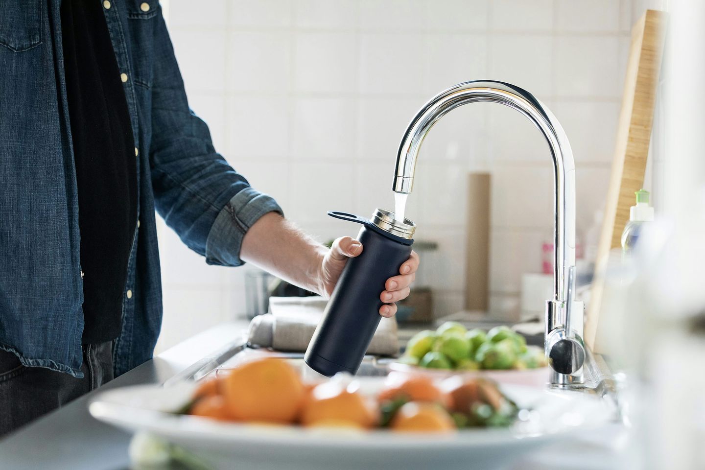 Männerhände füllen eine Trinkflasche mit Wasser