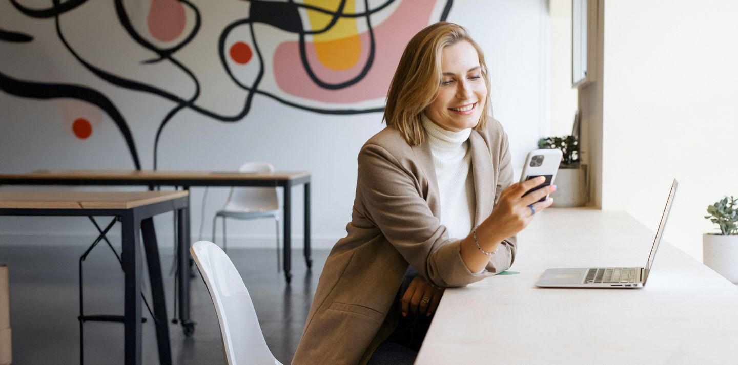 Frau sitzt mit dem Handy in der Hand und Laptop of dem Tisch @daria1life via Unsplash