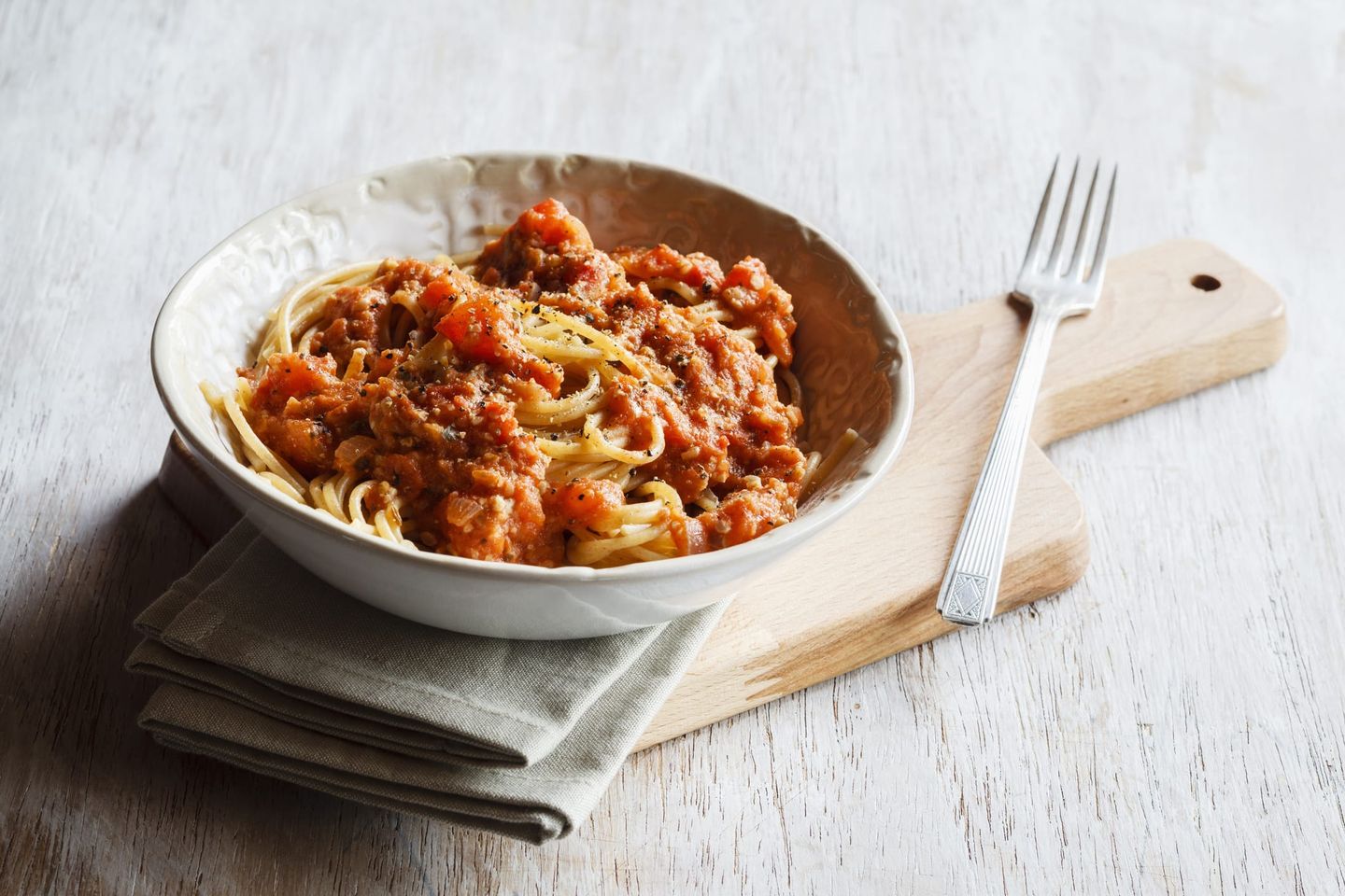 Vegane Spaghetti mit Tomatensauce, angerichtet in einer Schüssel auf einem Holzbrett mit Gabel und Stoffserviette