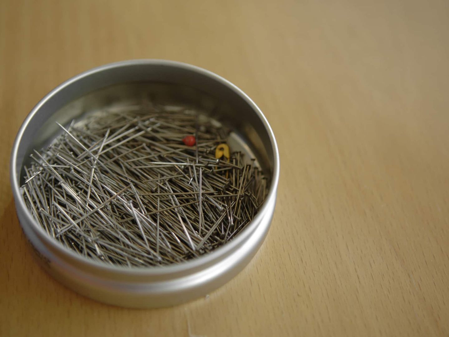 Runde Dose mit vielen Stecknadeln auf Holztisch. Getty