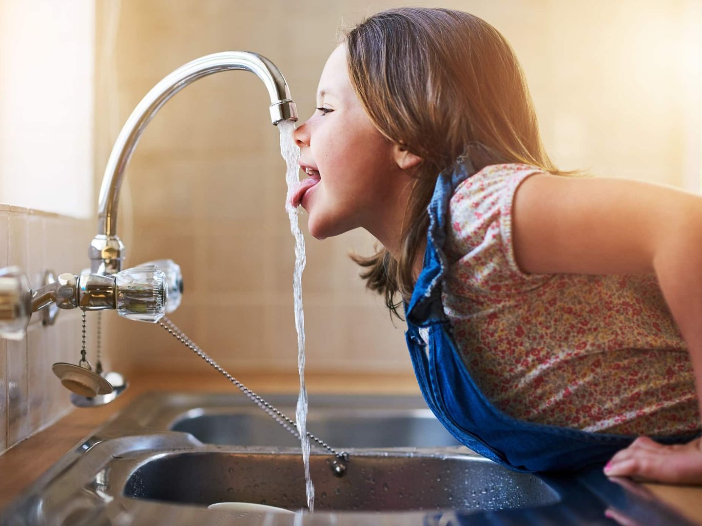 Ein Kind trinkt direkt aus dem Wasserhahn in der Küche. Getty
