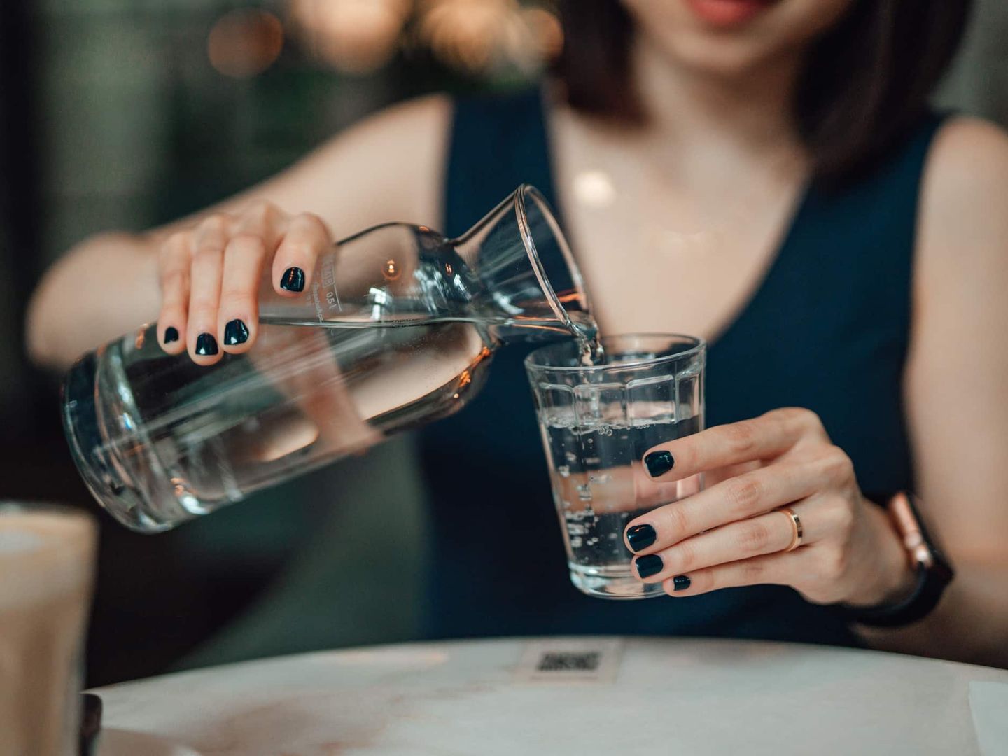 Eine Frau gießt Wasser aus einer Glaskaraffe in ein Trinkglas. Getty
