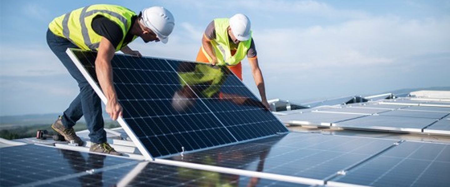 Zwei Installateure bringen Photovoltaik-Sonnenkollektoren auf dem Dach eines Unternehmens an. © ArtistGNDphotography via via Getty Images