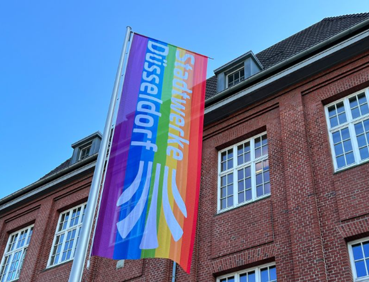 Vor dem Hauptsitz der Stadtwerke Düsseldorf weht eine Logofahne in Regenbogenfarben.