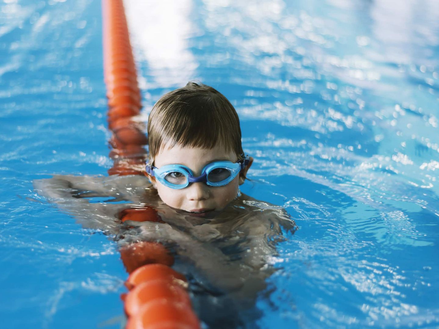 Junge mit Schwimmbrille hält sich im Wasser an der Bahnleine fest. Getty
