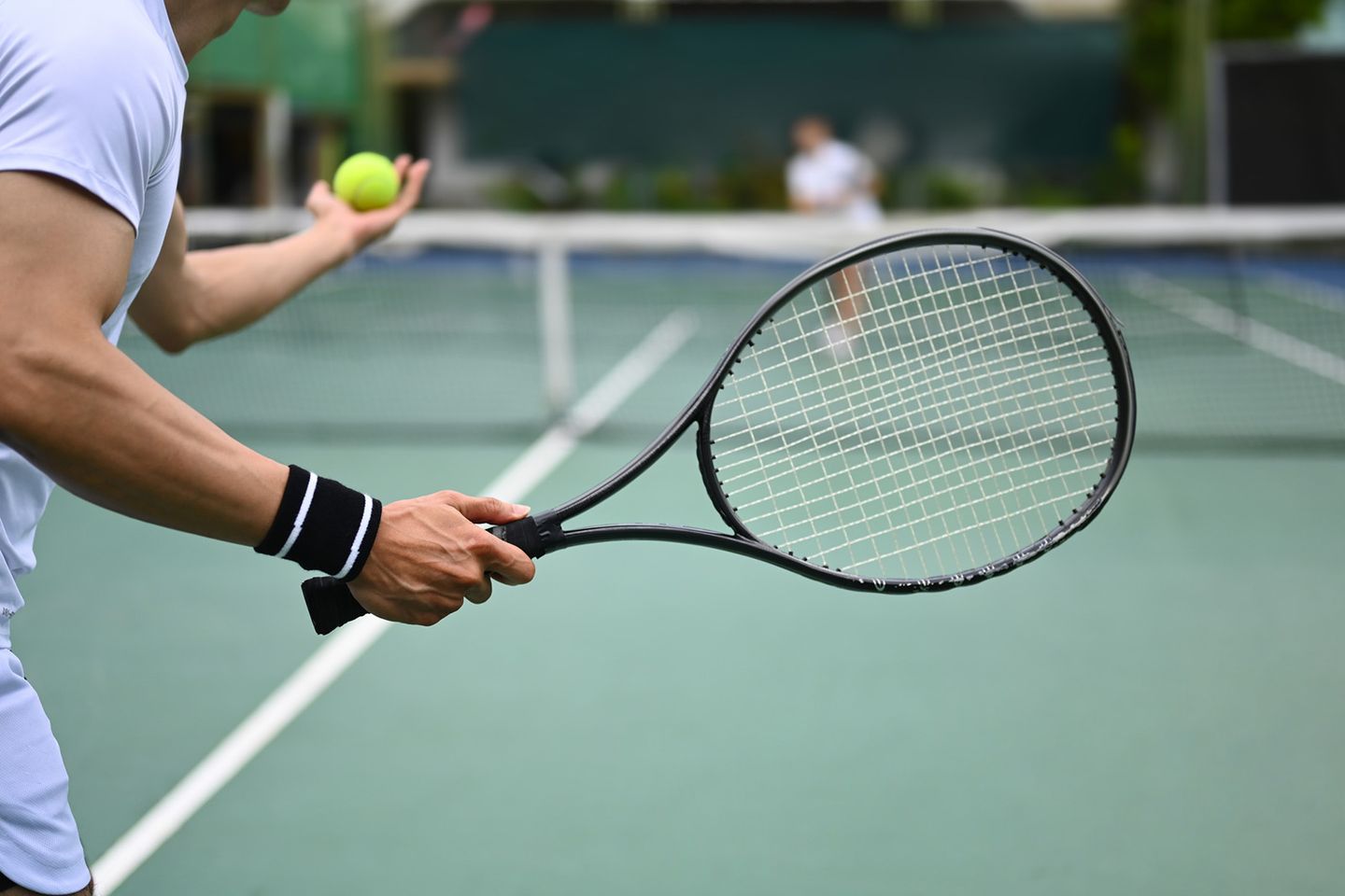 Nahaufnahme eines Tennisspielers in weißem Outfit, der sich auf einen Aufschlag vorbereitet und den Ball in der Hand hält.