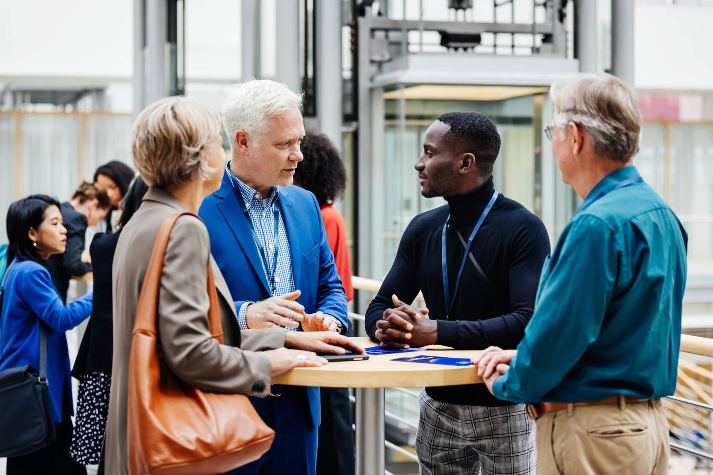 Geschäftsleute im Gespräch bei einem Networking-Event, Männer und Frauen diskutieren an einem Stehtisch. Getty