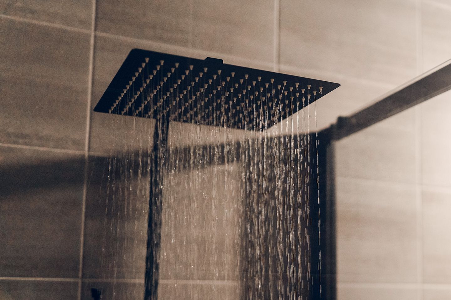 Eine moderne, quadratische Regendusche in einem gefliesten Badezimmer, aus der feine Wasserstrahlen fließen.