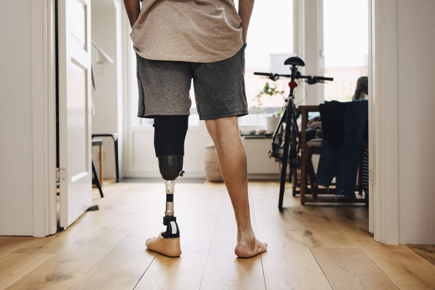 Mann mit Prothese steht barfuß in einer Wohnung neben einem Fahrrad. Getty