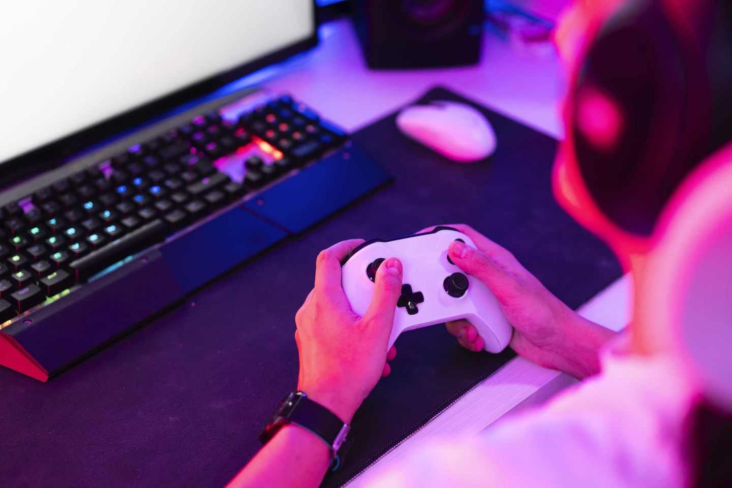 Junge Person spielt an einem Computer mit Gamepad in neonfarbenem Licht. Getty