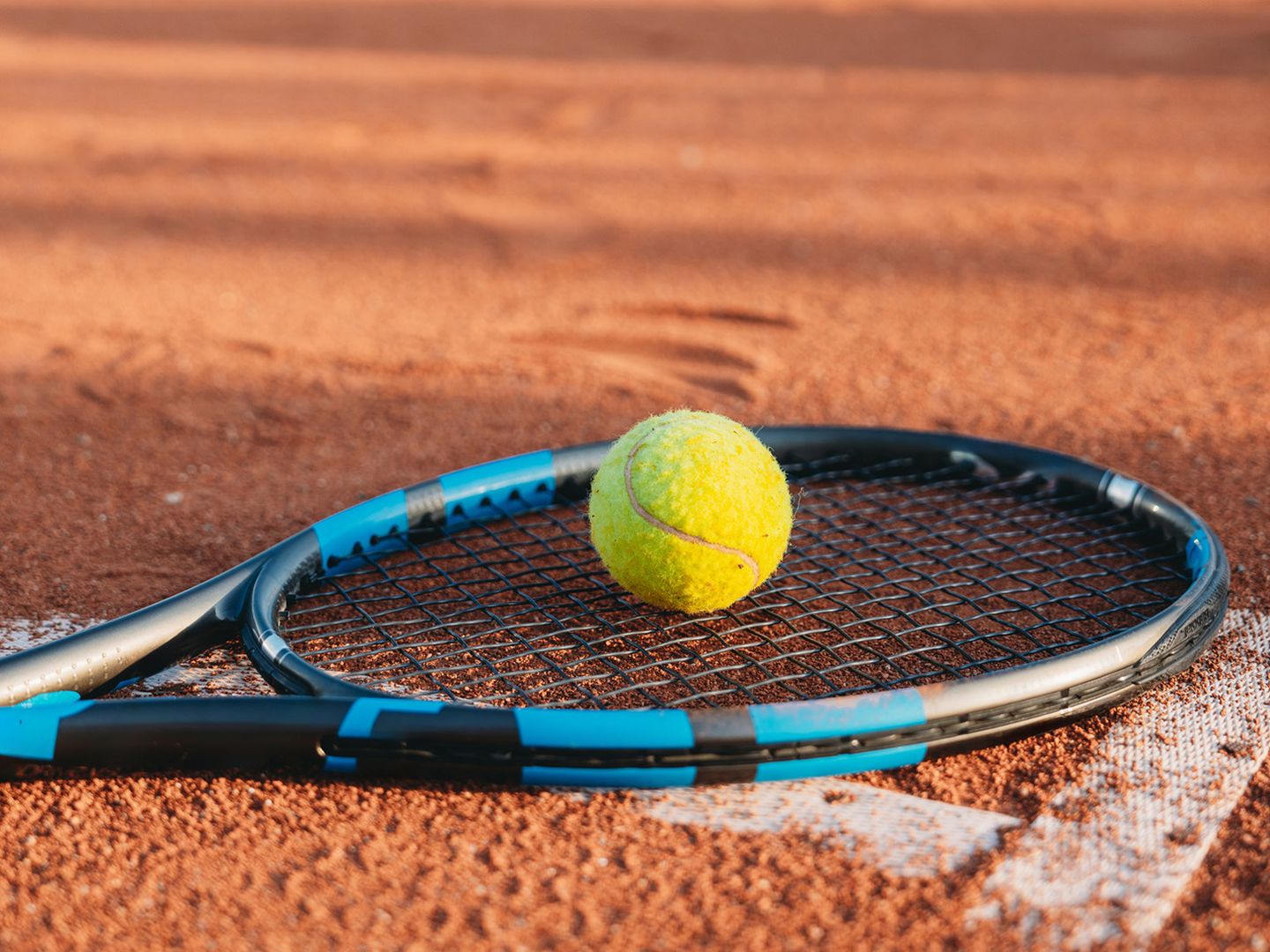 Ein gelber Tennisball liegt auf einem blauen und schwarzen Tennisschläger auf einem Sandplatz.