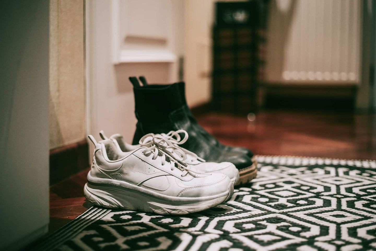 Ein Paar Schuhe, weiße Sneaker und schwarze Stiefel, steht ordentlich nebeneinander im Flur. Getty
