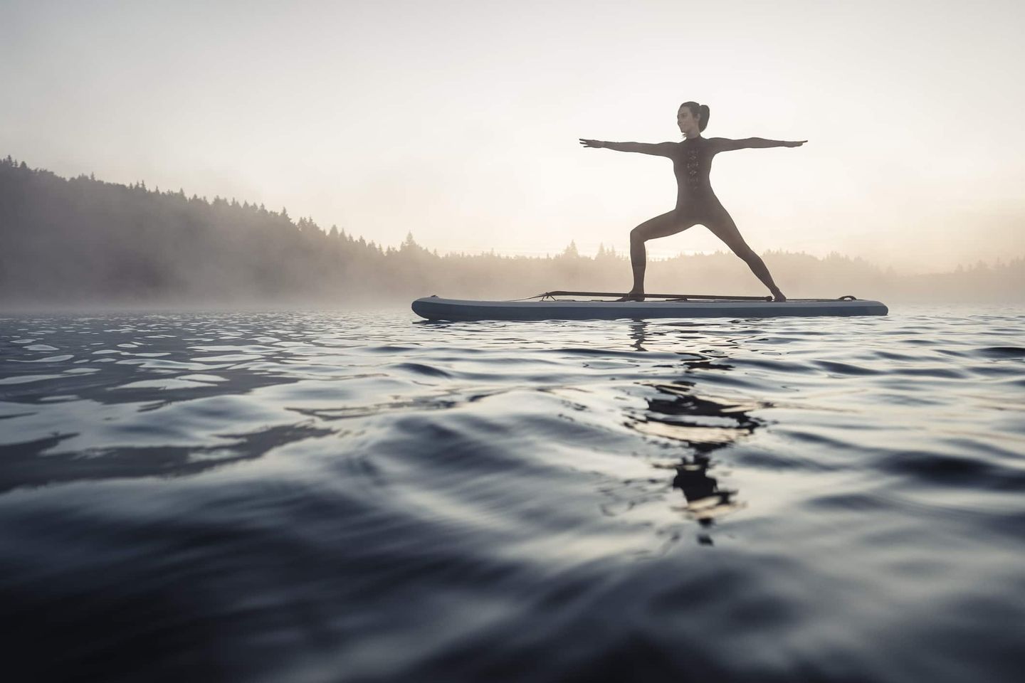 Frau macht Yoga-Übung im Krieger-Stand auf einem SUP-Board im See bei Nebel Getty