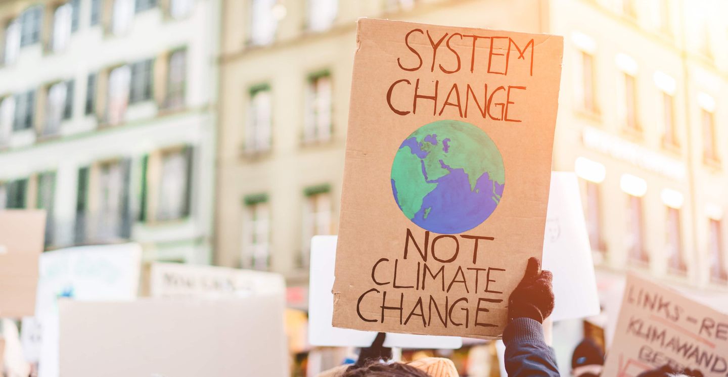 Pappschild mit Aufschrift „System Change, not Climate Change“ bei einer Klimademo. Getty