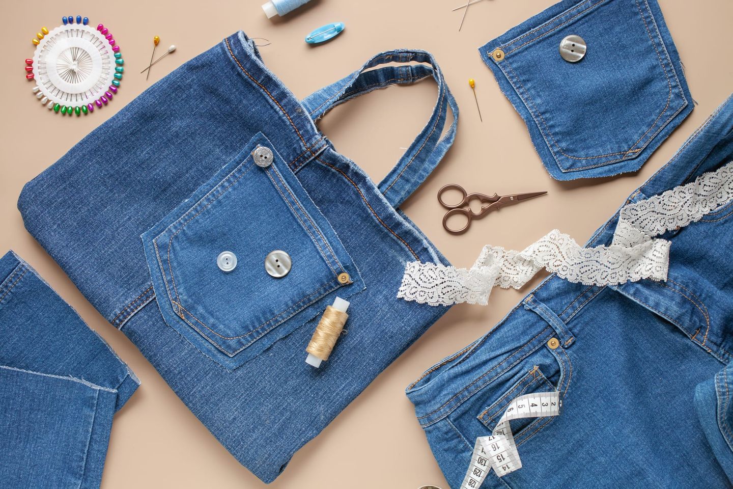 Eine selbstgenähte Tasche aus alter Jeans mit Gesäßtasche und dekorativen Knöpfen, umgeben von Nähzubehör wie Schere, Spitze und Maßband.