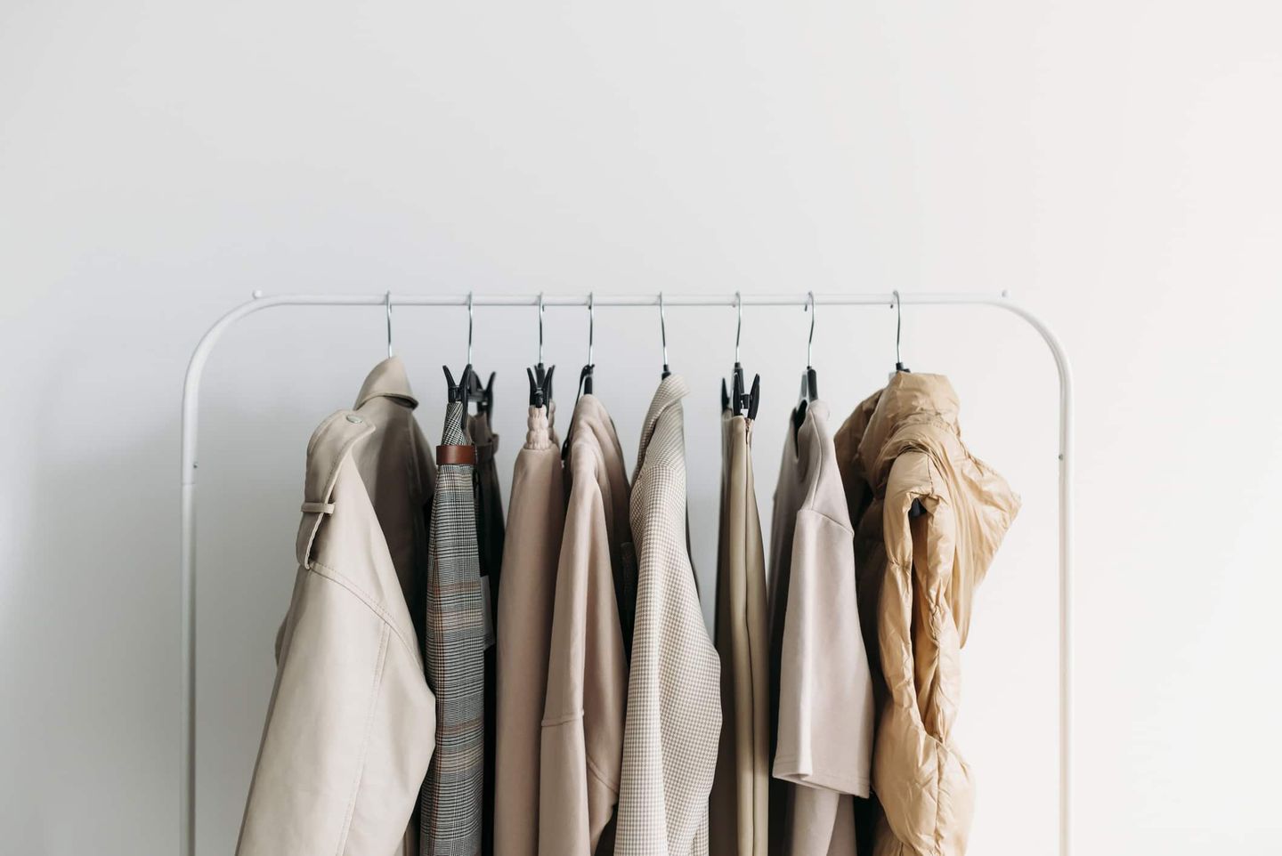 Minimalistische Capsule Wardrobe mit neutralen Kleidungsstücken, ordentlich auf einer Kleiderstange aufgehängt. Getty