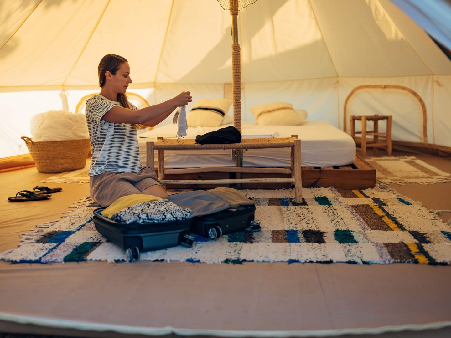 Frau packt im Inneren eines großen Glamping-Zeltes den Koffer aus Getty