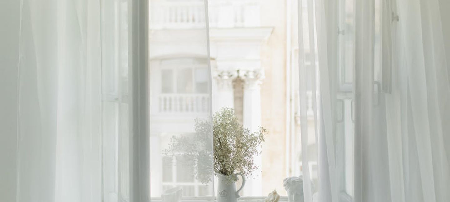 Richtig Lüften gegen Schimmel: Ein helles Zimmer mit transparenten Vorhängen und einem offenen Fenster.