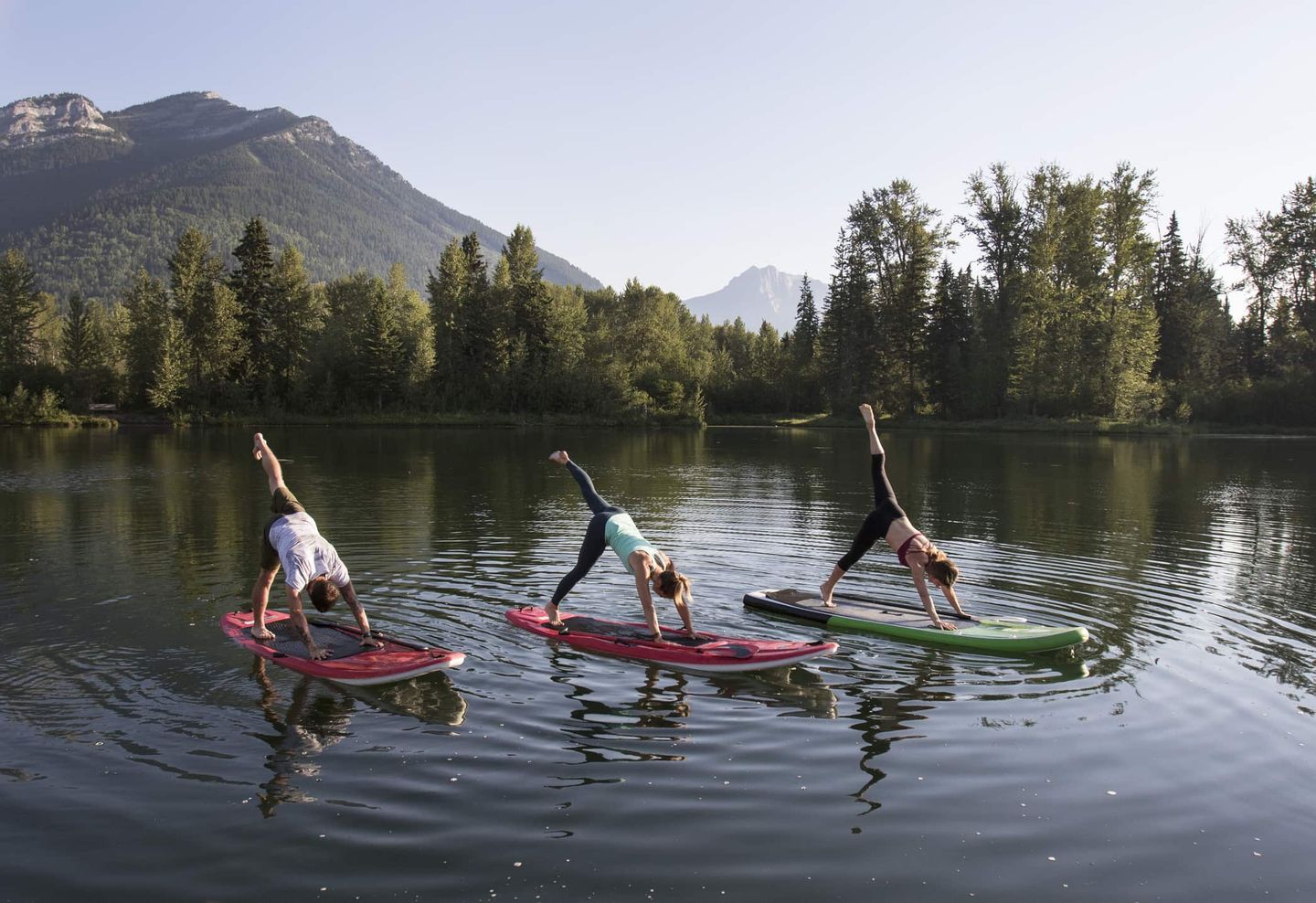 Gruppe von Menschen macht Yogaübungen auf SUP-Boards auf einem See mit Bergen im Hintergrund Getty