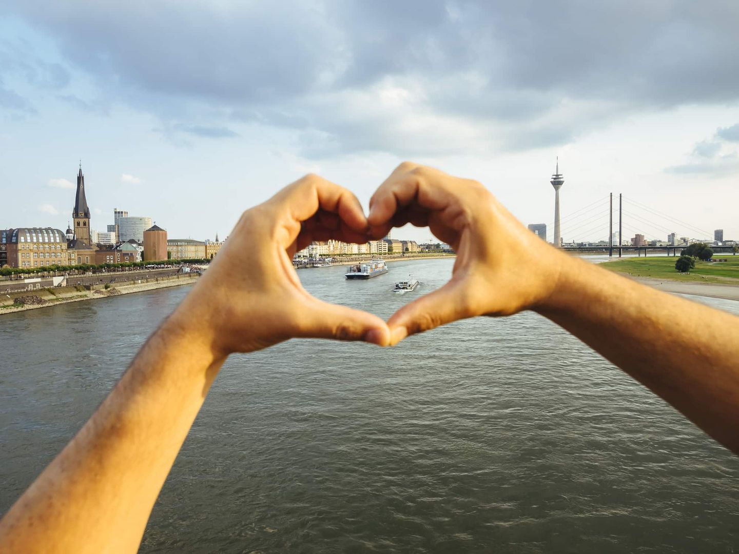 Hände formen ein Herz vor dem Blick auf den Rhein und den Rheinturm in Düsseldorf Getty