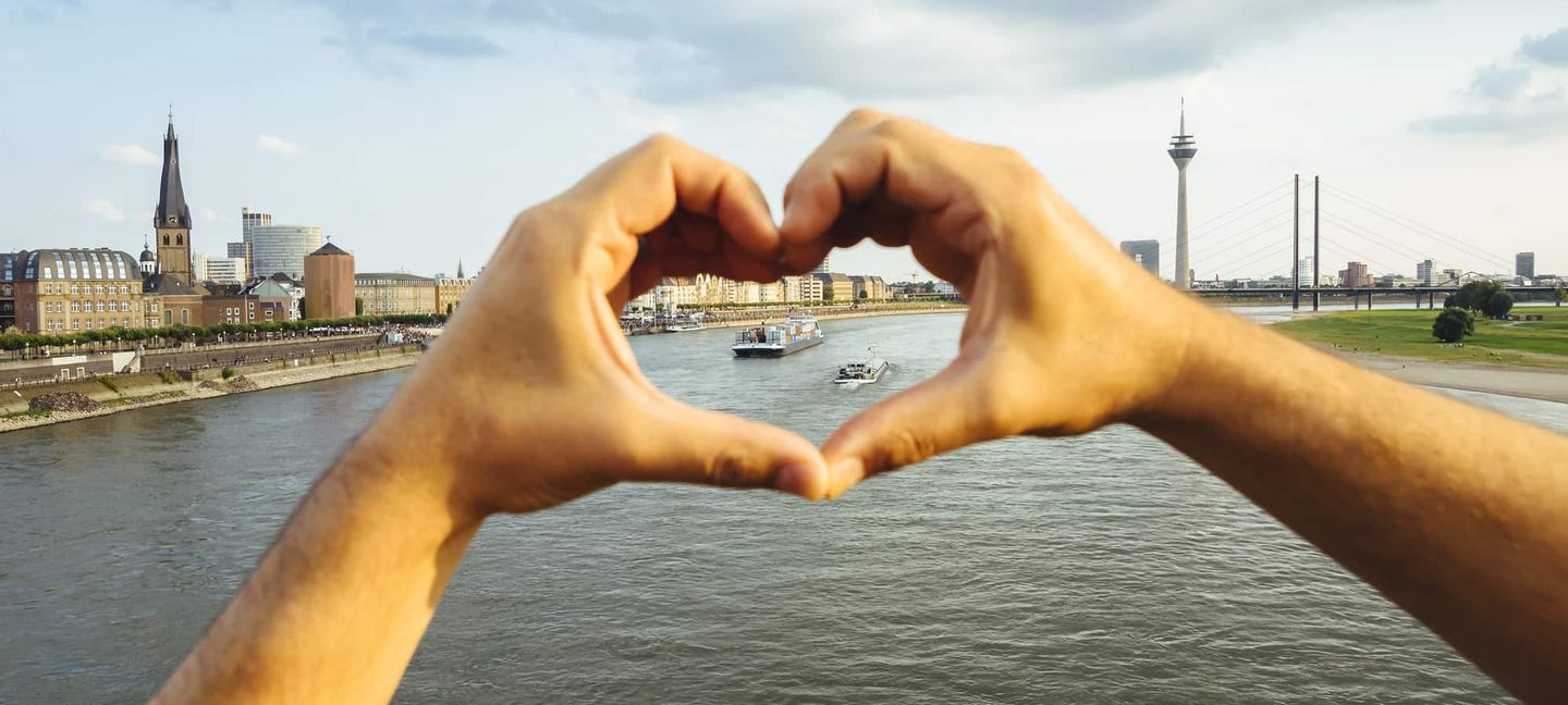 Hände formen ein Herz vor dem Blick auf den Rhein und den Rheinturm in Düsseldorf Getty