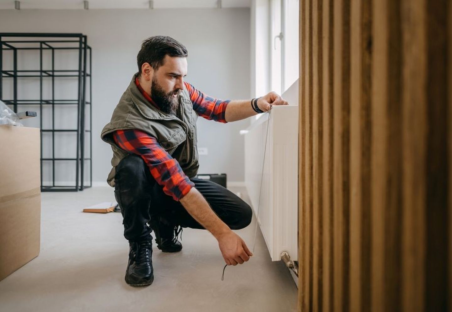 Ein Mann hockt vor einem Heizkörper und misst ihn aus. 