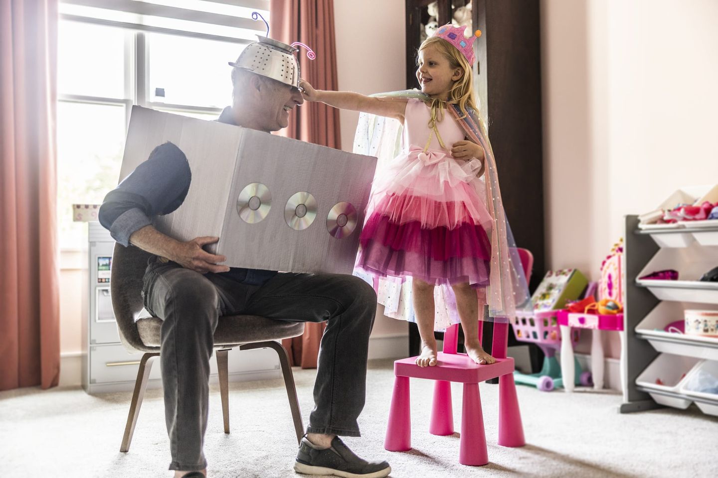 Ein Vater und seine Tochter verkleidet als Roboter und Prinzessin spielen gemeinsam Karneval in ihrem Wohnzimmer.